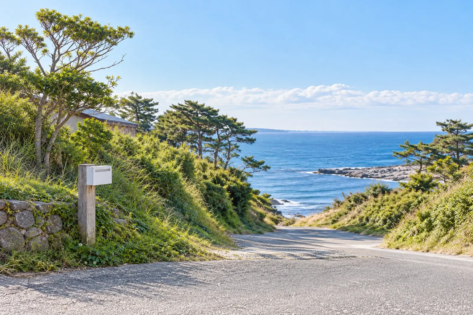 白い郵便受けの角と、海へ下りる細い道